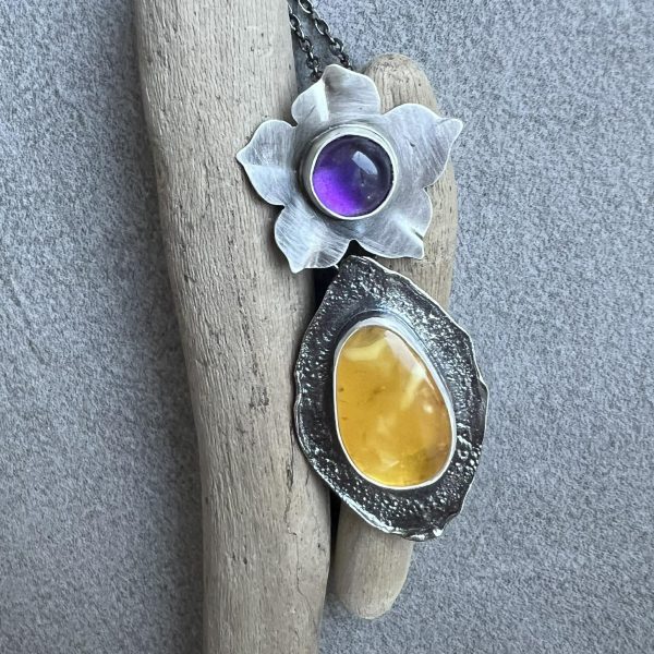 Wisiorek z bursztynem i ametystowym kwiatem prezentowany na kobiecym dekolcie. Ekskluzywna biżuteria srebrna Białystok, idealny pomysł na prezent dla koneserki unikatów
