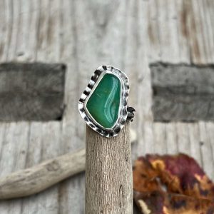 Srebrny pierścionek handmade z zielonym chryzoprazem o jabłkowym odcieniu. Surowa oprawa ze srebra przypominająca organiczne formy natury, tło stanowi drewno wyłowione z morza. Pierścionki z chryzoprazem