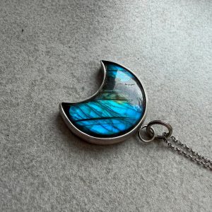 Lunula luna księżyc. Srebrny wisior w kształcie Lunuli półksiężyca z naturalnym szarym labradorytem wykazującym niebieską poświatę labradoryzacji. Kamień mocno zakuty w ciemne, oksydowane i matowe srebro próby 925. Słowiański amulet kobiecości i biżuteria artystyczna handmade od Kamyki Moniki.