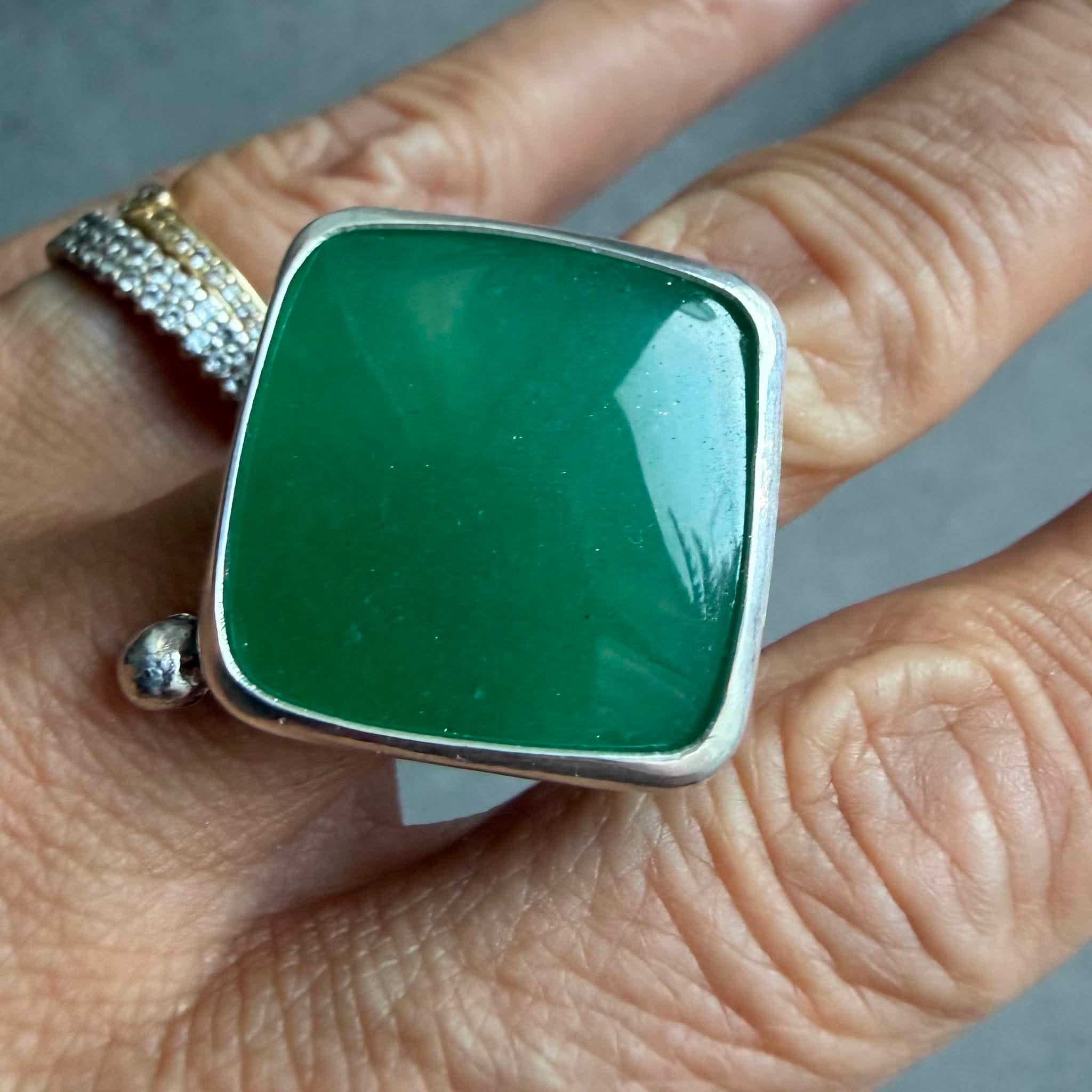 Kwadratowy pierścionek z zielonym awenturynem ze srebra 925 na dłoni. Zielony awenturyn kwadrat 22x22 mm gładki szlif ze srebrną kulką. Jasna polerowana kwadratowa oprawa i przyciemniana srebrna obrączka. Duży kwadratowy pierścionek z zielonym awenturynem regulowany Kwadratowy pierścionek z zielonym awenturynem ze srebra 925 na dłoni. Zielony awenturyn kwadrat 22x22 mm gładki szlif ze srebrną kulką. Jasna polerowana kwadratowa oprawa i przyciemniana srebrna obrączka. Duży kwadratowy pierścionek z zielonym awenturynem regulowany