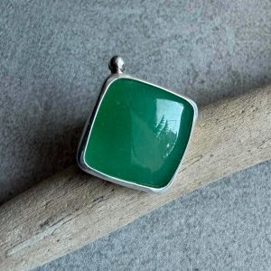 Kwadratowy pierścionek z zielonym awenturynem ze srebra 925 na dłoni. Zielony awenturyn kwadrat 22x22 mm gładki szlif ze srebrną kulką. Jasna polerowana kwadratowa oprawa i przyciemniana srebrna obrączka. Duży kwadratowy pierścionek z zielonym awenturynem regulowany