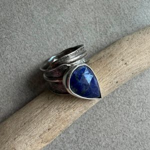 Lazuryt pierścionek fasetowany kropla ze srebra 925 na dłoni, Granatowy lapis lazuli kropla 18x12 mm z drobinkami pirytu, Regulowana srebrna obrączka jak ogon jaszczurki z lazurytem, Jasna srebrna oprawa fasetowanego kamienia lazurytu na przetartej obrączce