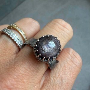 Rubin gwieździsty pierścionek. Rubin gwieździsty pierścionek w koronkowej oprawie ze srebra 925 na dłoni. Rubin gwieździsty 12x11 mm w srebrnej koronce połyskujący w świetle. Falowana i regulowana przecierana srebrna obrączka pierścionka z rubinem. Kunsztowna oprawa koronkowa z mocno oksydowanego srebra 925 z rubinem