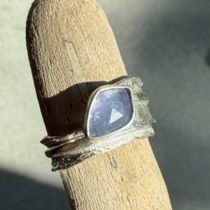 Tanzanit naturalny. Pierścionek z naturalnym fasetowanym tanzanitem na dłoni ze srebra 925. Fasetowany tanzanit naturalny 10x7 mm z inkluzjami w polerowanej oprawie. Fakturowana regulowana srebrna obrączka jak ogonek jaszczurki z tanzanitem. Tanzanit umieszczony wzdłuż fakturowanej oksydowanej obrączki ze srebra