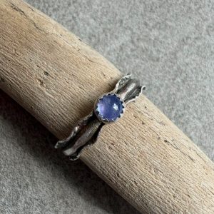 Tanzanit pierścionek regulowany fala. Tanzanit pierścionek regulowany fala na dłoni ze srebra 925. Okrągły tanzanit 4 mm w ząbkowanej oprawie ze srebra. Falowana szeroka 5 mm srebrna obrączka pierścionka z tanzanitem. Polerowane, ząbkowane i przyciemniane srebro 925 wokół tanzanitu.